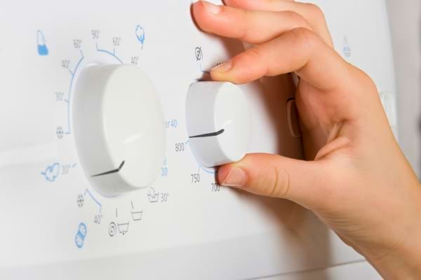 Main féminine réglant les boutons d’un lave-linge pour lancer un programme d’entretien. 