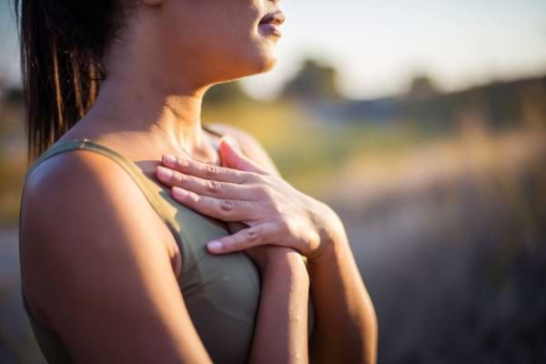 Une femme pose ses mains sur sa poitrine en respirant profondément dehors.