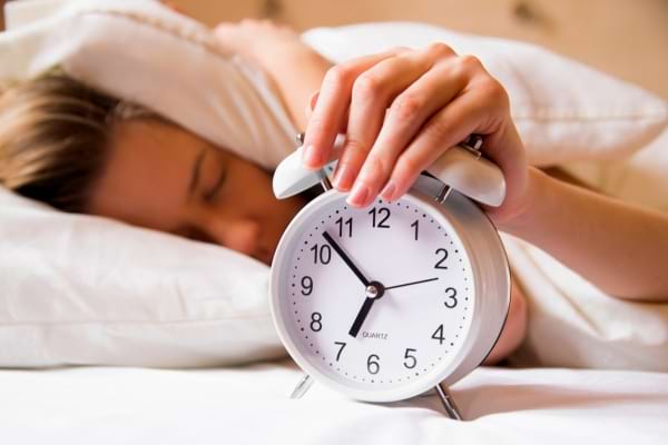 Une personne tente d’éteindre un réveil alors qu’elle est encore au lit, illustrant un réveil difficile.