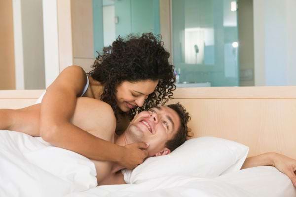 Une femme sourit à son partenaire enjoué dans le lit.