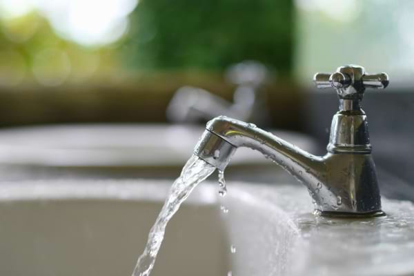 Robinet métallique avec eau qui coule doucement dans un lavabo, en contexte domestique naturel.  