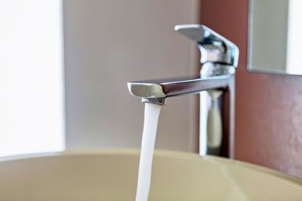 Un robinet moderne laisse couler un filet d’eau dans un lavabo beige.