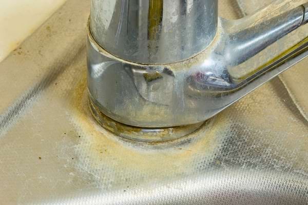 Base d’un robinet sale et incrustée de calcaire jaunâtre dans un évier en inox.