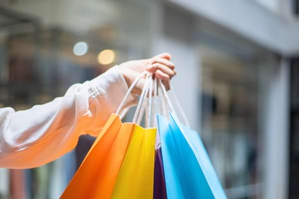 Main tenant plusieurs sacs de courses multicolores dans une galerie marchande.