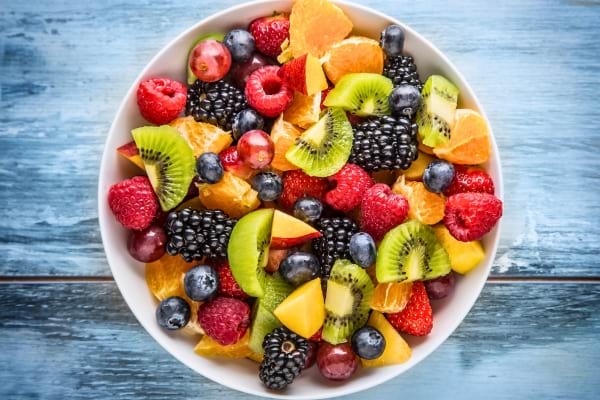 Une salade de fruits variée dans un bol blanc posé sur une table bleue.