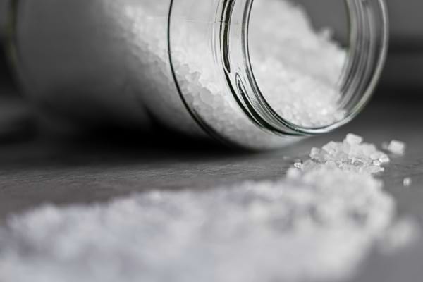 Un pot renversé laisse échapper du gros sel sur une surface grise.