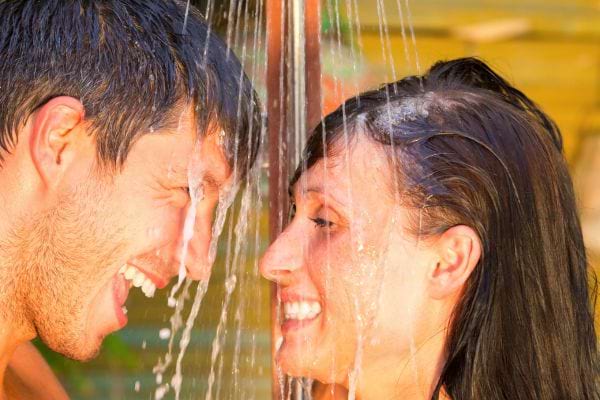 Un couple joue sous une douche extérieure en souriant.