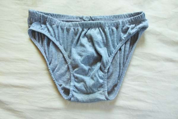 Slip gris en coton froissé, posé à plat sur un drap blanc.