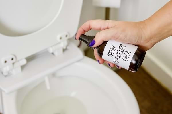 Une main qui pulvérise un spray anti-odeurs de caca dans la cuvette des WC.