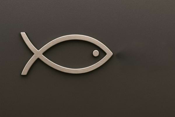Symbole en métal représentant un poisson chrétien sur fond gris foncé.