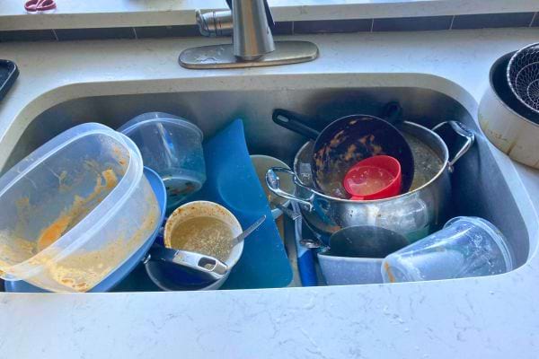Évier rempli de boîtes en plastique, casseroles et ustensiles sales.