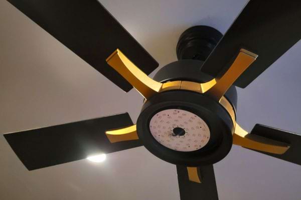 Ventilateur moderne noir et doré avec design futuriste et lumière centrale.