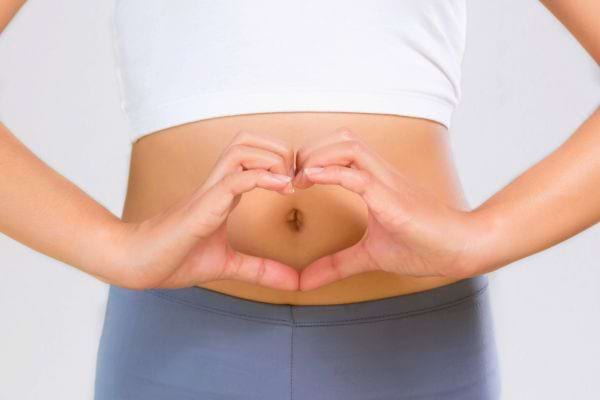 Mains formant un cœur sur un ventre plat.