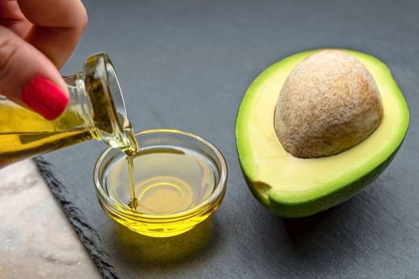 Huile d’avocat versée dans une coupelle, posée près d’un avocat frais.