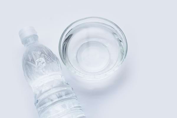 Bouteille et bol remplis de vinaigre blanc posés sur un fond clair.