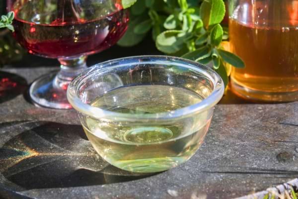 Un petit bol en verre transparent rempli de vinaigre, entouré d'autres liquides colorés.