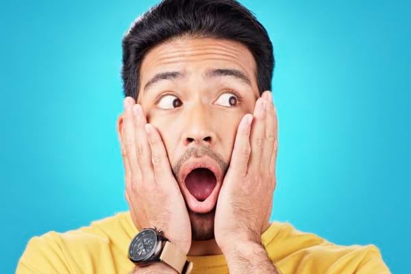 Homme surpris en t-shirt jaune, les mains sur les joues, fond bleu vif.