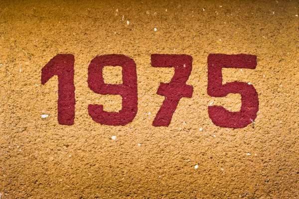 Chiffres rouges "1975" peints sur un mur jaune texturé. 