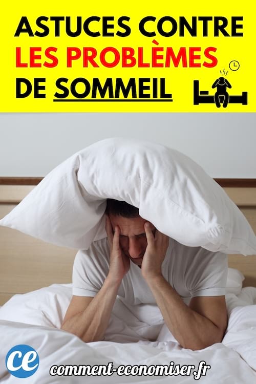 Un homme assis sur un lit se tient la tête entre les mains avec un oreiller sur la tête, visiblement perturbé par l'insomnie.