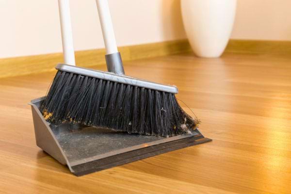 Un balai noir posé dans une pelle à poussière sur un sol en bois.