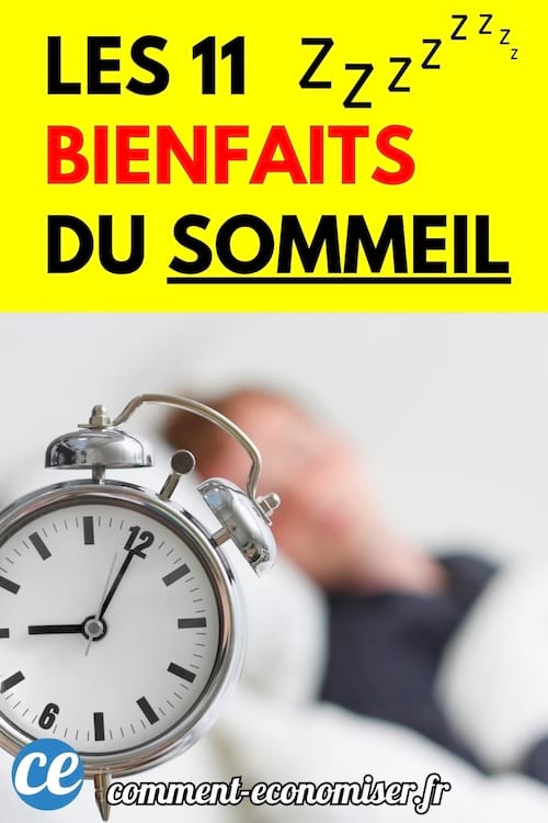 Un réveil argenté posé sur un lit avec une personne floue en arrière-plan en train de dormir.