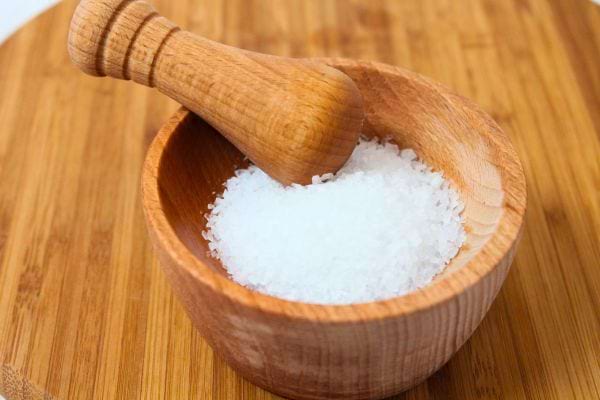 Un petit bol en bois rempli de gros sel blanc.