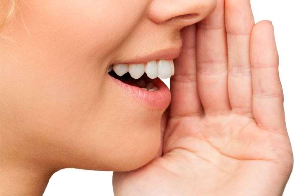 Une femme souriante parle en tenant sa main devant sa bouche.