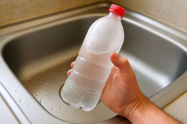 Une main tient une bouteille en plastique remplie d’eau, prête à l’utilisation.
