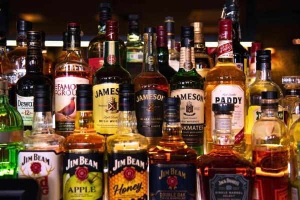 Plusieurs bouteilles d’alcool, principalement du whisky, sont alignées sur une étagère dans un bar.