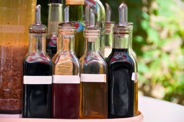 Plusieurs bouteilles de vinaigre de différentes couleurs sont réunies sur un plateau à l’extérieur.