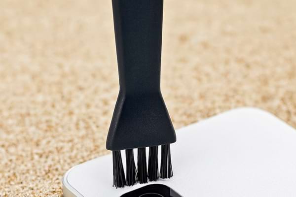 Une petite brosse nettoie l’objectif d’un smartphone plein de sable.