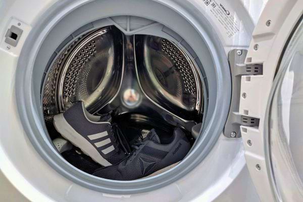 Une paire de baskets noires est placée dans le tambour de la machine.