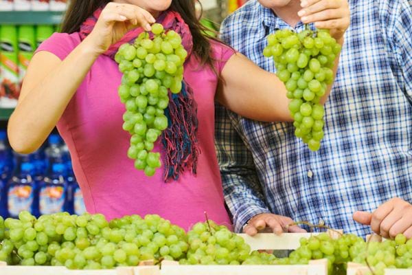 Deux personnes comparent des grappes de raisins verts sur un étalage de marché.