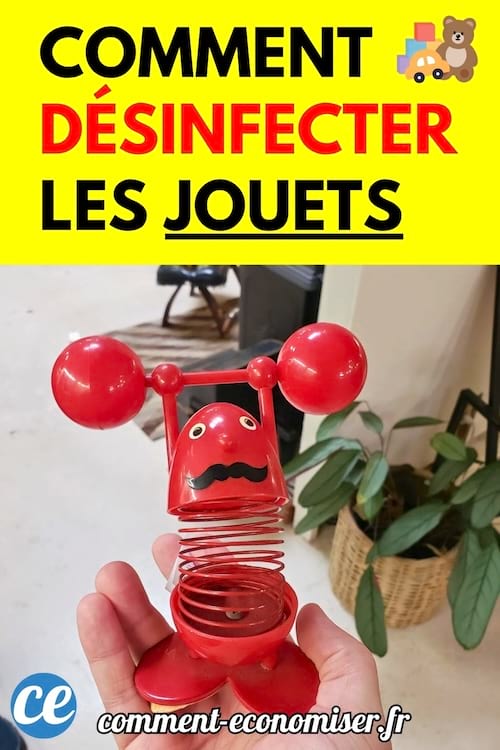 Une main tient un petit jouet rouge en plastique avec un ressort et des bras levés dans un salon avec des plantes en arrière-plan.