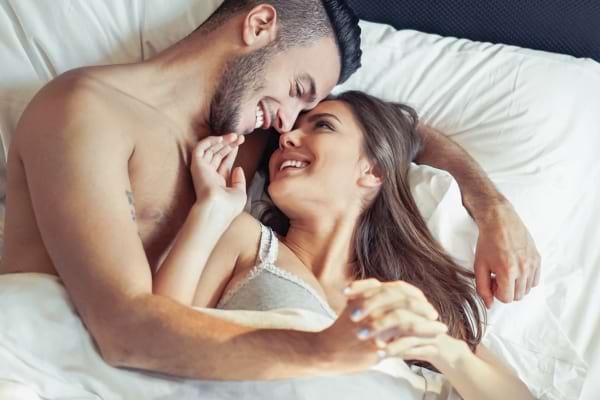 Couple enlacé et souriant dans un lit.