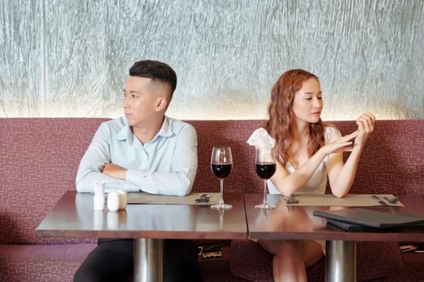 Un couple est assis au restaurant, chacun regarde de son côté, silence et froideur.