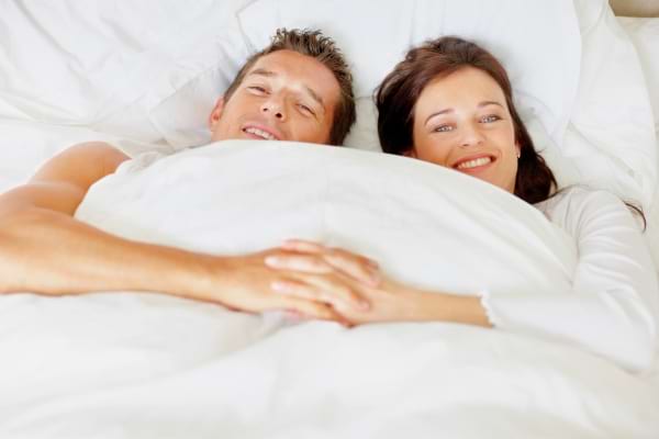 Couple détendu allongé sous une couette blanche.