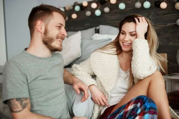 Un couple discute joyeusement sur un lit, ambiance détendue et pleine de complicité.