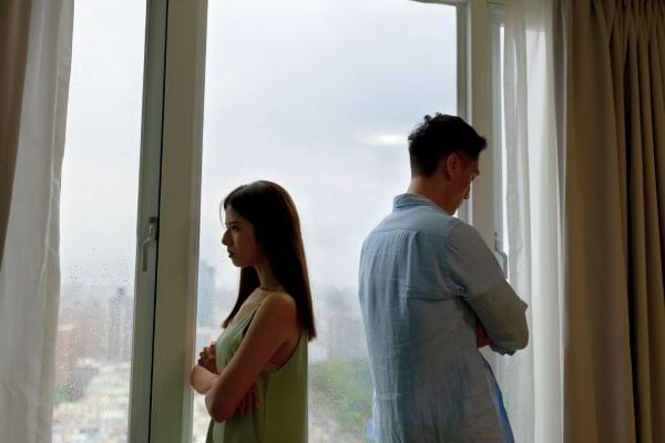 Couple dos à dos près d’une fenêtre, visiblement en froid.