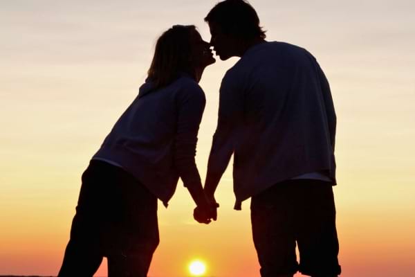 Un couple amoureux se tient la main au coucher du soleil, sur le point de s’embrasser tendrement.