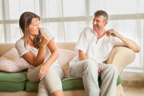 Un couple rit aux éclats en parlant sur le canapé.