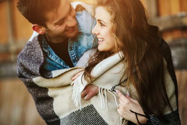 Un homme et une femme rient ensemble, enveloppés dans une grande couverture, regard complice.