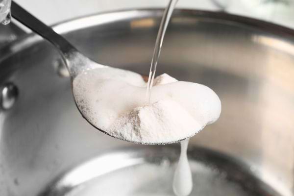 Cuillère de poudre blanche réagissant au contact de l’eau versée.