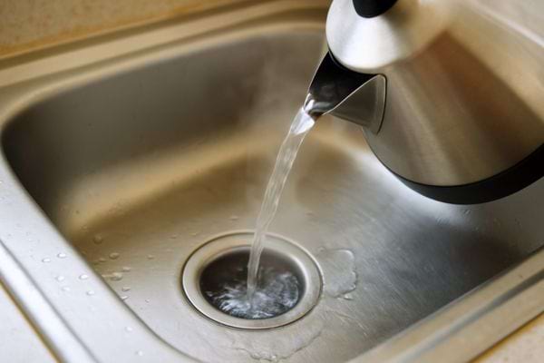 Une bouilloire verse de l’eau bouillante dans la canalisation de l’évier.