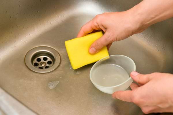 Une éponge et un bol de liquide sont utilisés pour nettoyer l’évier.