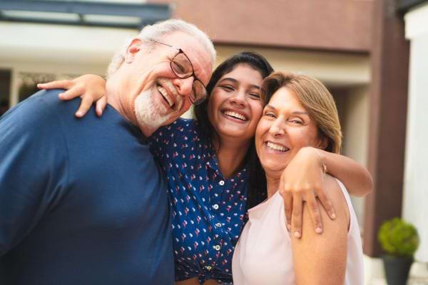 Une famille souriante s’enlace joyeusement devant la maison.