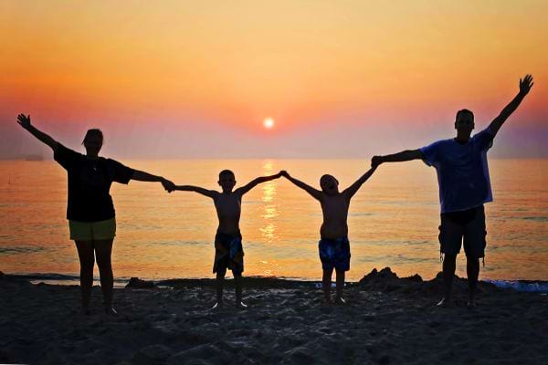 Silhouettes d’une famille bras levés au coucher de soleil.