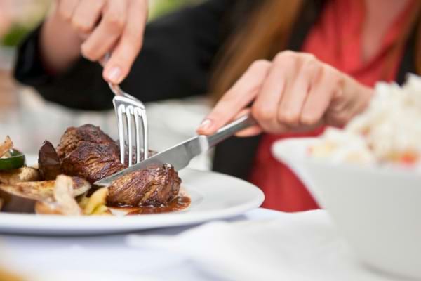 Femme coupant un morceau de viande dans son assiette avec fourchette et couteau.