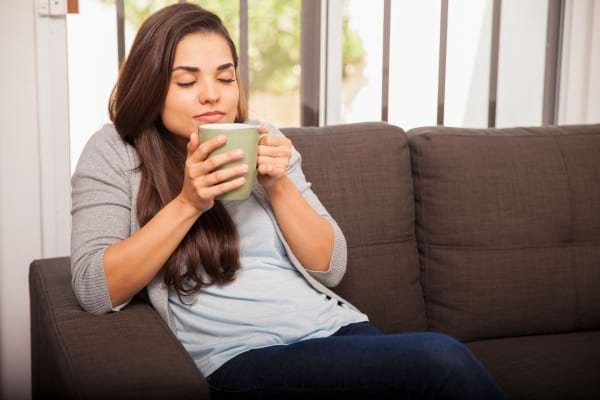 Une femme détendue savoure une boisson chaude, assise sur un canapé.