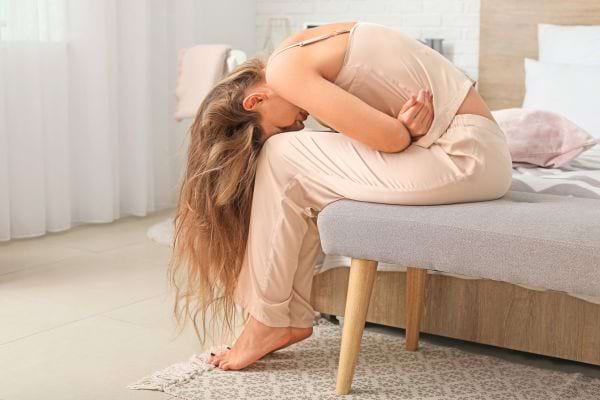 Femme assise, recroquevillée, souffrant physiquement.